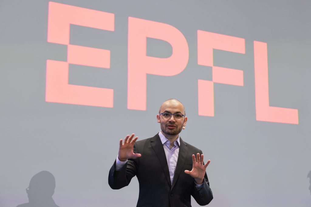 Demis Hassabis on stage in a suit and with an EPFL logo in the background. Demis Hassabis 2023 EPFL/Alain Herzog - CC-BY-SA 4.0