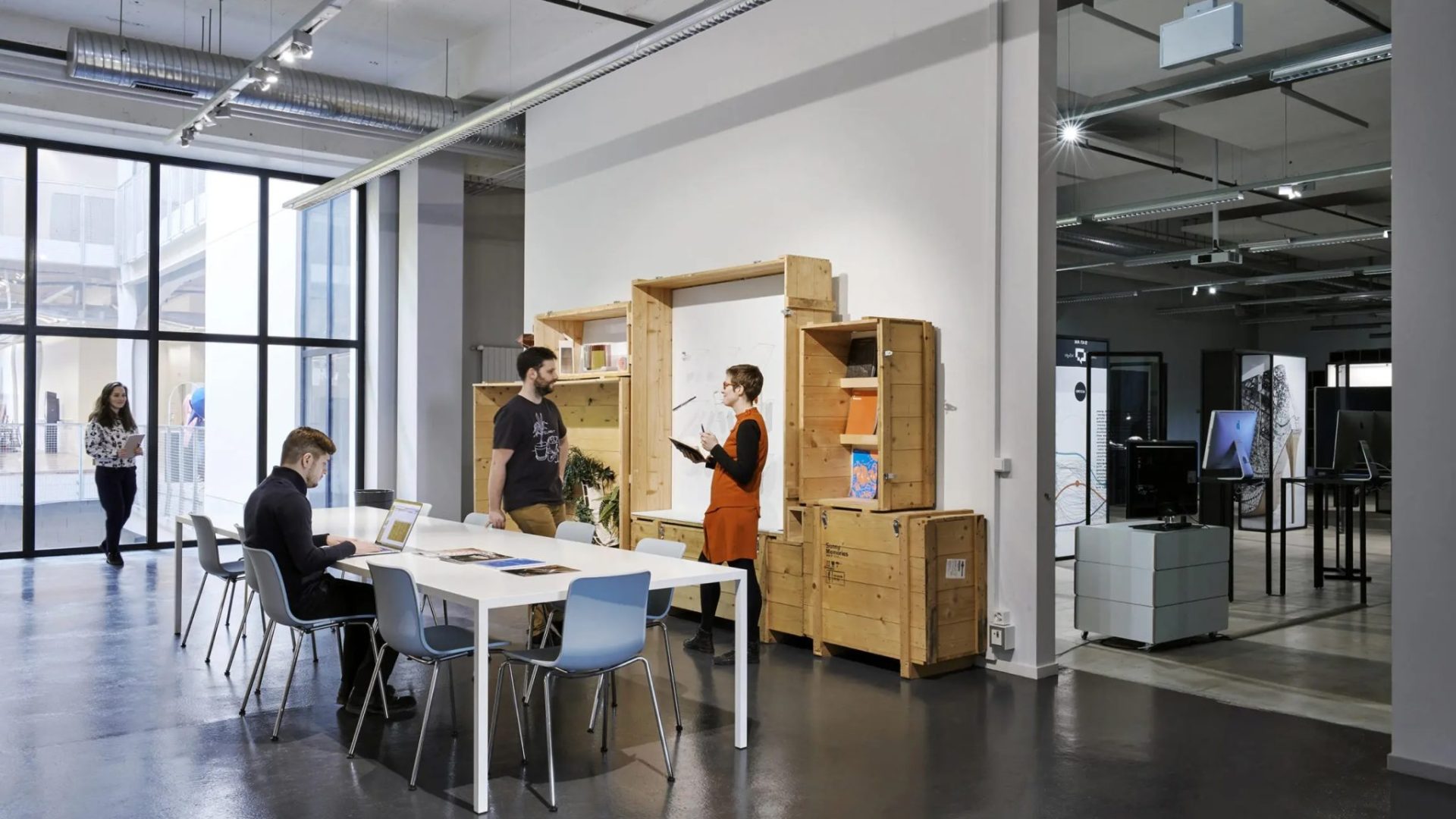 EPFL-Ecal Lab. Une personne est assise à une table, deux autres discutent debout © Daniela-Tonatiuh
