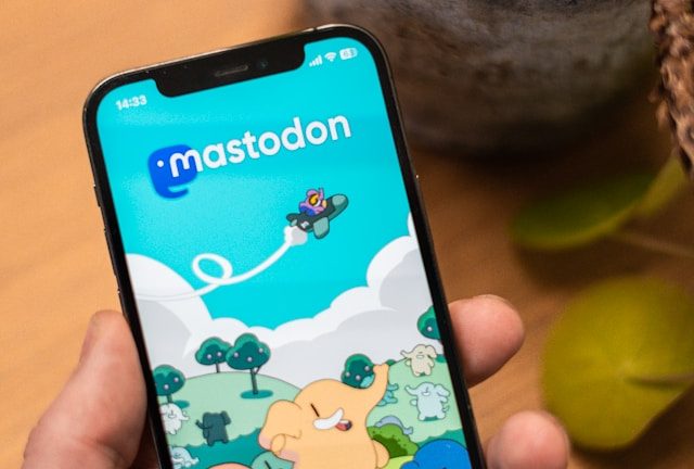 Une main tenant un téléphone avec la page d'accueil de l'instance Mastodon.social